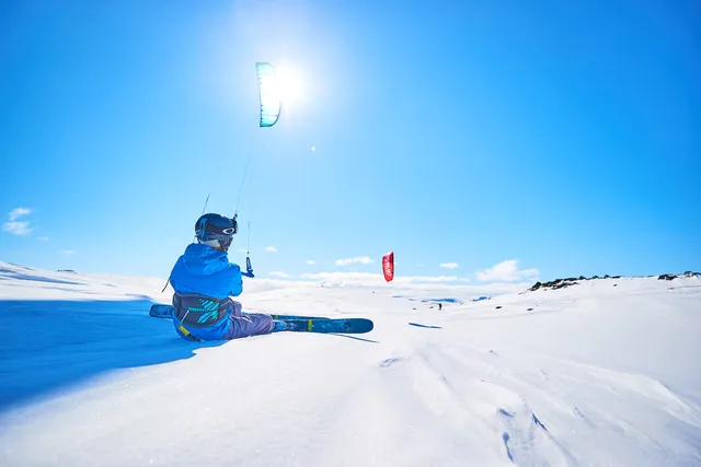 A snowkiter crossing bright snow under a blue sky.