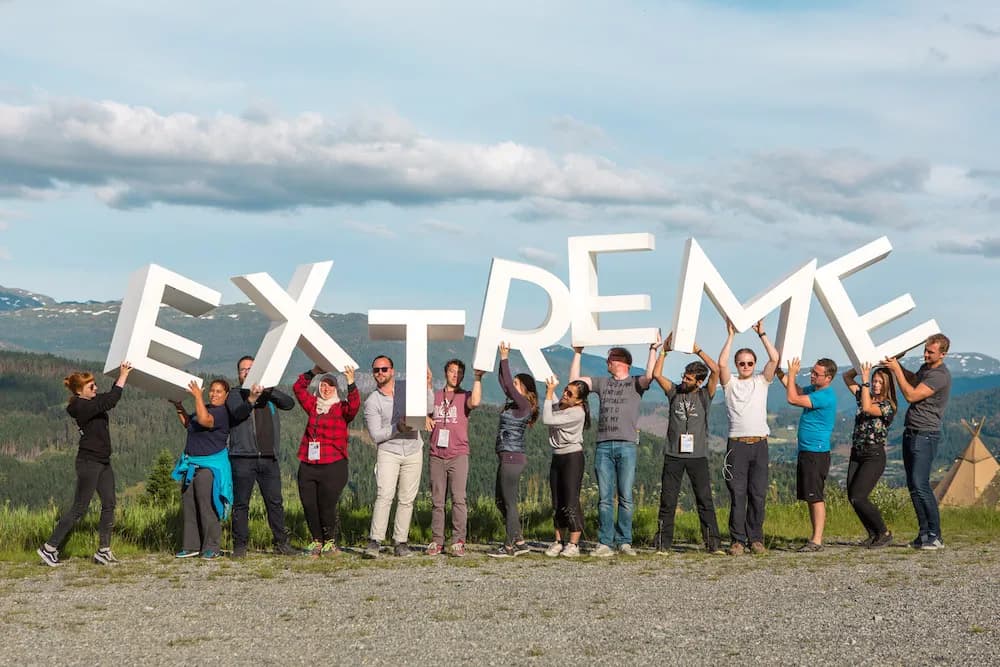About fifteen people on a summer mountainside hold up giant white letters spelling EXTREME.