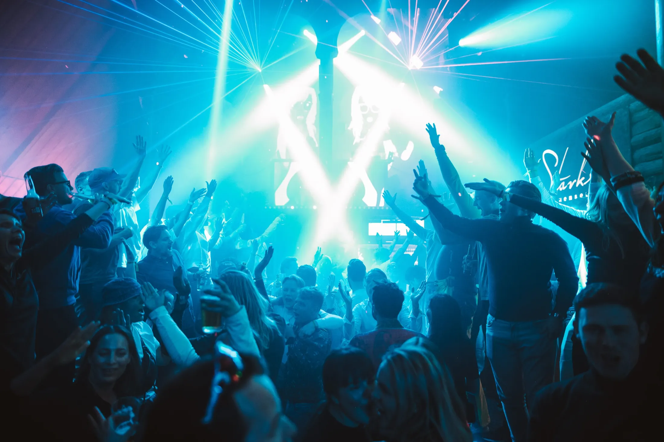 A packed dance floor with hands in the air under blue and white lasers at Stavkroa.