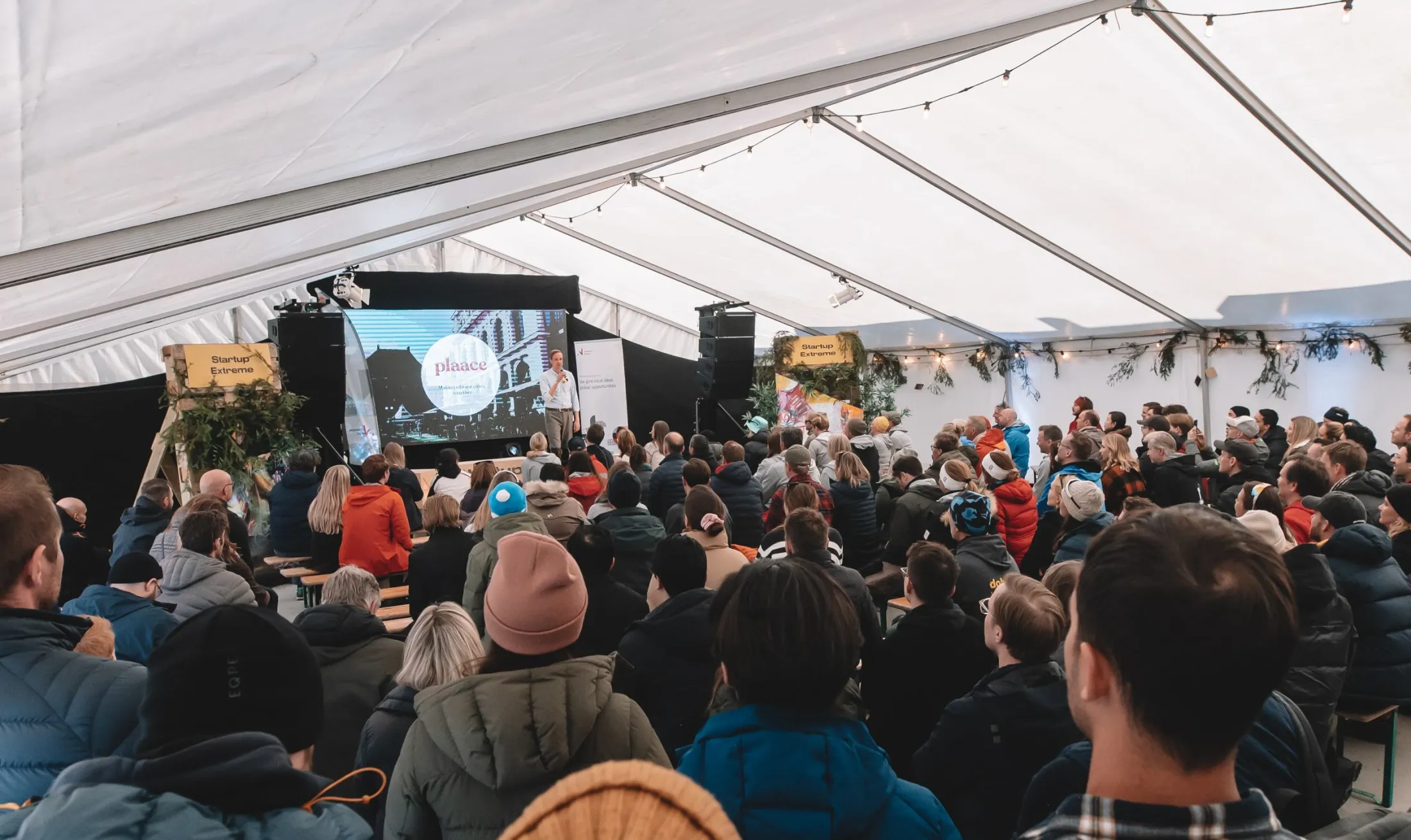 A full white tent, the audience facing a speaker on the stage.
