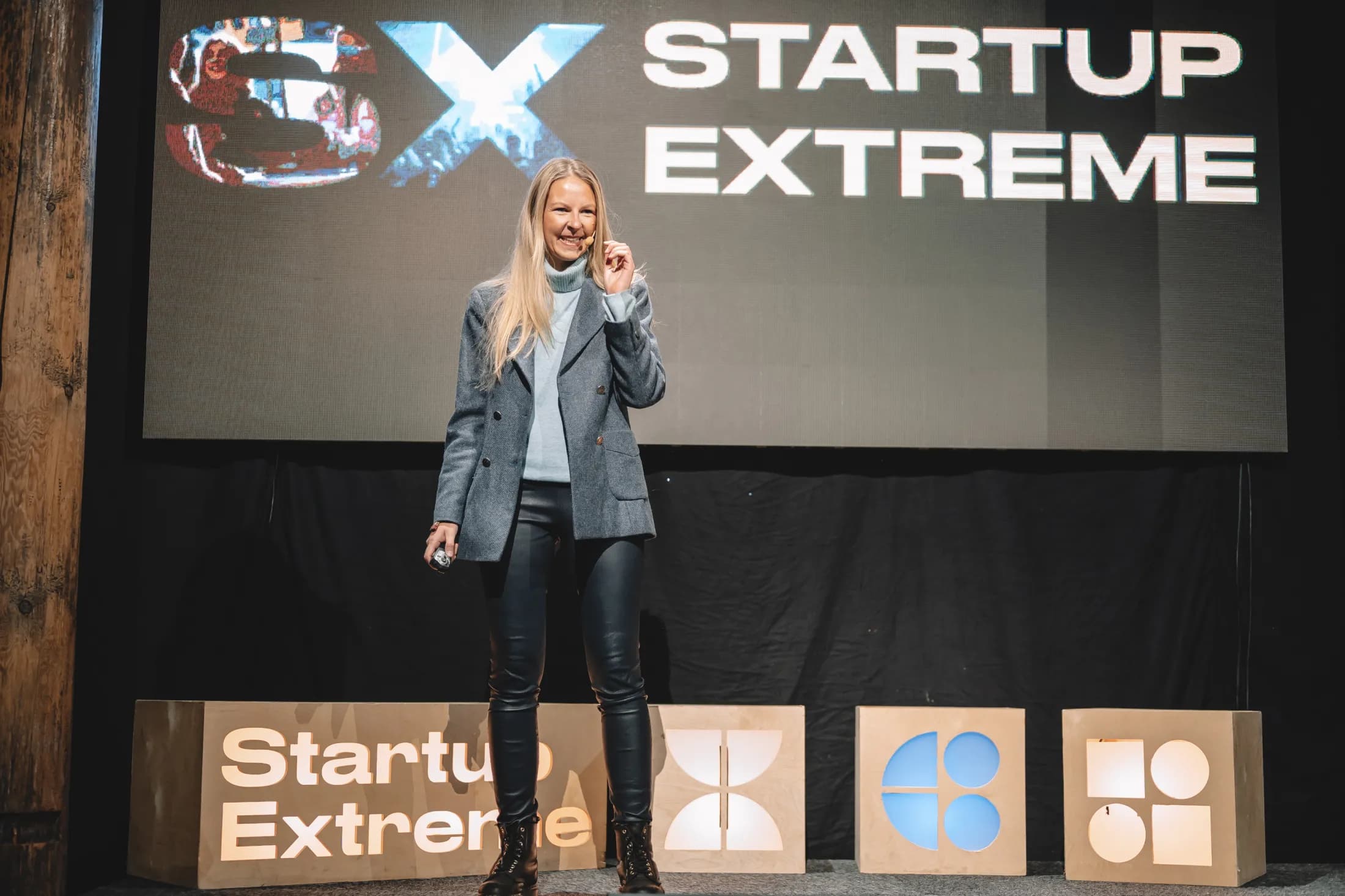 A woman on stage in front of a big Startup Extreme screen and the SX letter cubes.