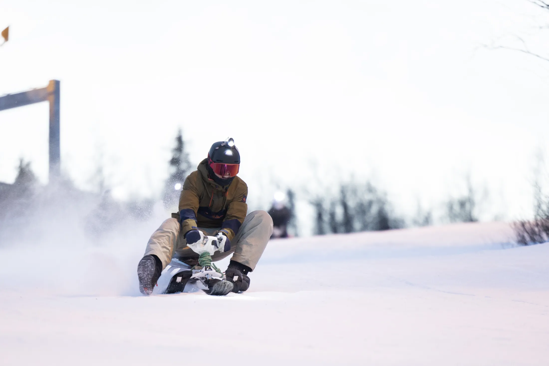 Someone on a toboggan at speed down a snowy slope, snow spraying.