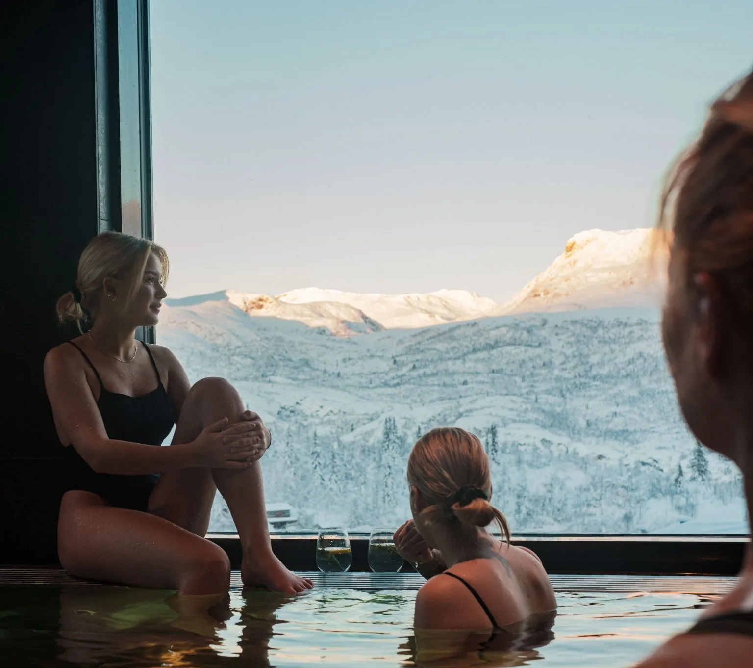 Two women in an infinity pool looking out over snow-covered mountains.