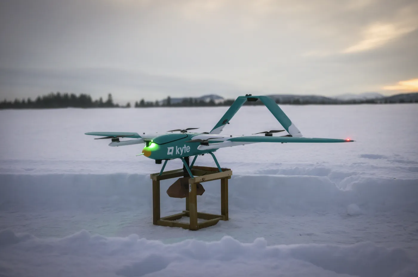 An Aviant delivery drone on a wooden stand on a snowy frozen lake at dusk.